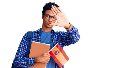 Afrika kökenli Amerikalı genç bir adam sırt çantası takıyor. Elinde İspanyol bayrağı var ve dur işareti yapıyor. Ciddi ve kendinden emin bir ifadeyle. 