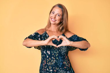 Orta yaşlı İspanyol kadın, gündelik giysiler giyip, sevgiyle gülümsüyor. Kalp sembolü ve elleri ile şekil veriyor. romantik kavram. 