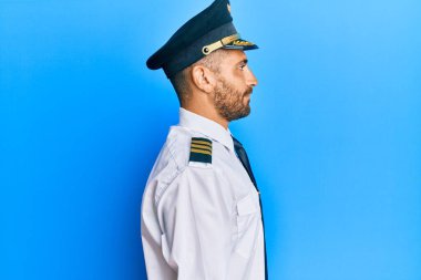 Sakallı, uçak pilotu üniforması giyen yakışıklı, rahat bir görünüm takınan, kendine güvenen bir gülümsemesi olan yakışıklı bir adam.. 