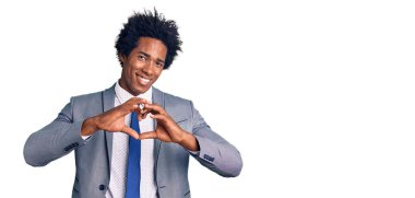 Afro saçlı, iş ceketi giyen, aşık bir şekilde gülümseyen, elleriyle kalp sembolü yapan yakışıklı Afro-Amerikan bir adam. romantik kavram. 