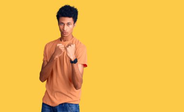 Genç, Afro-Amerikalı, günlük kıyafetler giymiş, yumruk savunma hareketleriyle dövüşmeye hazır, kızgın ve üzgün yüzlü, sorundan korkan. 