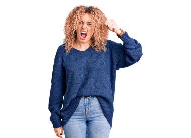 Kıvırcık saçlı, sıradan bir kazak giyen, sinirli ve sinirli genç bir kadın öfkeyle bağırırken yumruğunu kaldırıyor. öfke ve agresif konsept. 