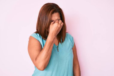 Middle age brunette hispanic woman wearing casual clothes tired rubbing nose and eyes feeling fatigue and headache. stress and frustration concept. 