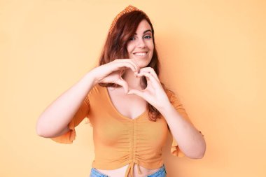 Genç ve güzel bir kadın, gündelik kıyafetler giyip, aşıkken gülümsüyor ve elleriyle kalp sembolü yapıyor. romantik kavram. 