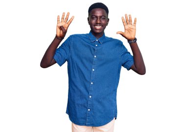 Genç, Afro-Amerikalı, günlük kıyafetler giymiş, dokuz numaralı parmaklarıyla işaret ederken, kendinden emin ve mutlu bir şekilde gülümsüyor.. 