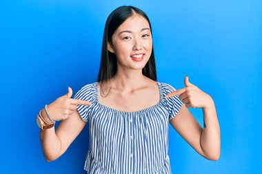 Sıradan çizgili tişört giyen genç Çinli bir kadın. Kendine güvenen, yüzünde gülümseme olan, kendini gururlu ve mutlu gösteren bir kadın.. 