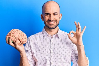 Beyni tutan genç yakışıklı kel adam parmaklarıyla imza atıyor, gülümseyerek mükemmel bir sembol oluşturuyor. 