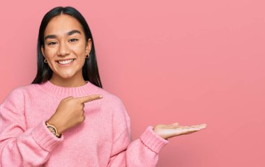 Günlük kışlık süveter giyen genç Asyalı kadın kameraya hayret ediyor ve gülümsüyor.. 