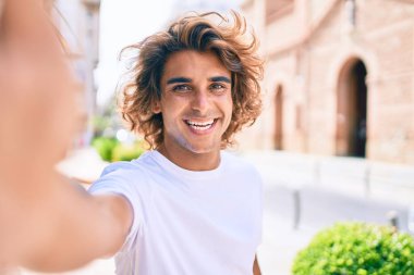 Genç, yakışıklı İspanyol gülümseyen adam şehrin caddesinde fotoğraf çekerken mutlu oluyor.