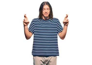 Uzun saçlı, sıradan çizgili tişört giyen yakışıklı beyaz adam umut ve gözleri kapalı bir şekilde gülümseyerek işaret ediyor. Şans ve batıl inançlar. 