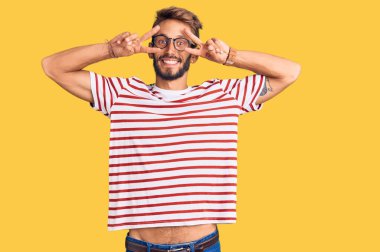 Sakallı, sıradan kıyafetler giyen, gözlüklü, barış sembolü takan, yüzünde gülümsemeyle zaferi gösteren yakışıklı sarışın adam. 