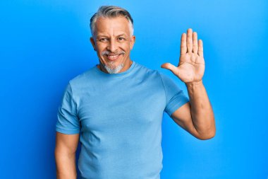 Orta yaşlı, gri saçlı, günlük kıyafetler giyen, beş numaralı parmaklarıyla işaret eden, kendinden emin ve mutlu bir adam.. 