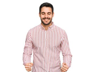 İş gömleği giyen genç İspanyol adam çok mutlu ve heyecanlı. Kolları havada, gülümseyen ve başarı için çığlık atan kazanan bir jest yapıyor. kutlama konsepti. 