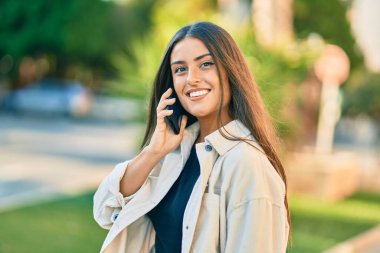 Genç İspanyol kız gülümsüyor. Parktaki akıllı telefondan konuşarak mutlu oluyor..