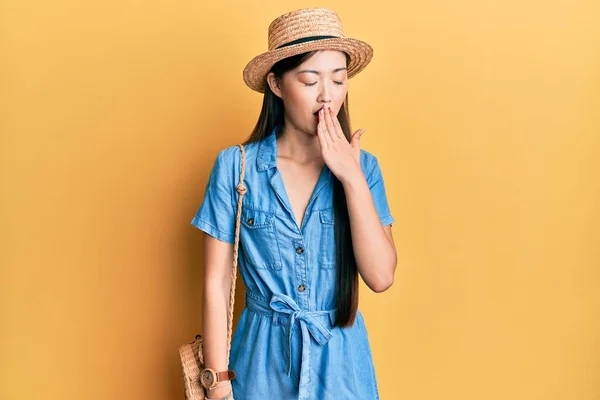 Young chinese woman wearing summer hat bored yawning tired covering mouth with hand. restless and sleepiness.