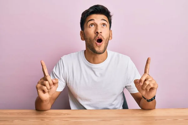 Joven Hombre Guapo Con Camiseta Blanca Casual Sentado Mesa Asombrado — Foto de Stock