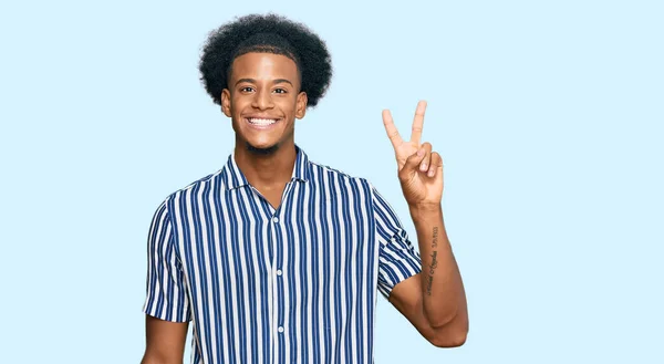 アフリカ系アメリカ人の男性は 勝利のサインをするカメラで幸せそうな顔をした笑顔でカジュアルな服を着ています — ストック写真