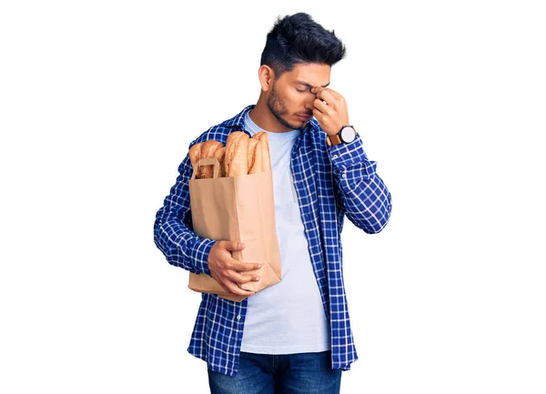 Guapo Joven Latinoamericano Sosteniendo Bolsa Papel Con Pan Cansado Frotando —  Fotos de Stock