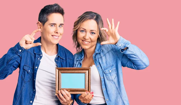 Couple Women Holding Empty Frame Smiling Confident Gesturing Hand Doing — Stock Photo, Image