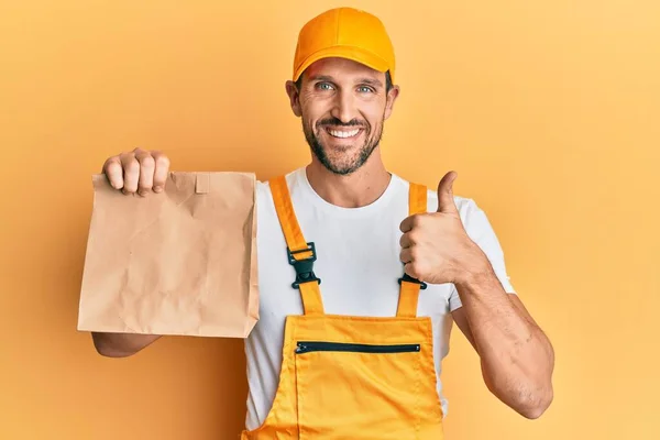 Joven Repartidor Guapo Sosteniendo Llevar Bolsa Papel Sonriendo Feliz Positivo — Foto de Stock