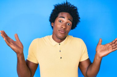 Yakışıklı Afro saçlı, sıradan kıyafetler giyen, kolları açık ve kafası karışmış, hiçbir fikri olmayan, şüpheli yüzlü Afro-Amerikan bir adam.. 