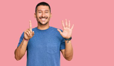 Dövmeleri olan yakışıklı bir adam gündelik giysiler giyer ve altı numaralı parmaklarıyla işaret ederken kendinden emin ve mutlu gülümserdi.. 