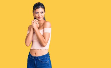 Gündelik kıyafetler giyen genç ve güzel bir kadın gergin ve heyecanlı elleri çenesinde yan tarafa bakıyor. 