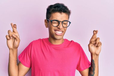 Pembe arka planda gözlük takan yakışıklı Afrikalı Amerikalı genç adam umut ve gözlerin kapalı bir şekilde gülümseyerek işaret ediyor. Şans ve batıl inançlar. 