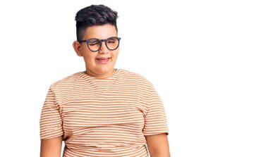 Günlük kıyafetler giyen ve gözlüklü küçük çocuk kameraya seksi bir ifadeyle bakıyor, neşeli ve mutlu bir yüzle.. 