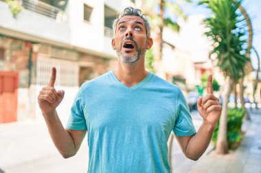 Şehrin caddesinde günlük giysiler giyen orta yaşlı, gri saçlı bir adam şaşkın şaşkın bakıyor, parmaklarıyla işaret ediyor ve kollarını kaldırıyordu.. 
