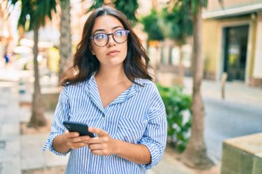 Şehirde akıllı telefon kullanan ciddi bir suratı olan genç İspanyol iş kadını..