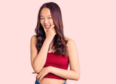 Gündelik kıyafetler giyen genç, güzel Çinli kız kameraya bakıyor kollarını kavuşturup gülümsüyor ve çenesini kaldırıyor. Olumlu düşünmek. 