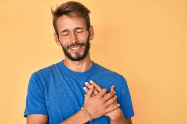 Sakallı, sıradan kıyafetler giyen, göğsünde elleri kapalı, yüzünde minnet ifadesi olan yakışıklı beyaz bir adam. sağlık kavramı. 