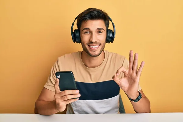 Young Handsome Man Using Smartphone Wearing Headphones Doing Sign Fingers — Stock Photo, Image