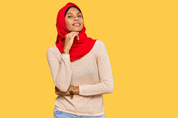 伝統的なイスラム教のヒジャーブスカーフを身に着けている若いアフリカ系アメリカ人女性は カメラが交差した腕とあごに上げ手で笑顔で自信を持って見ています ポジティブな — ストック写真
