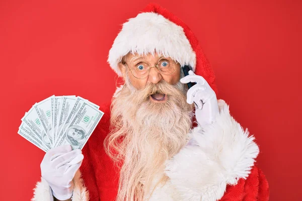 Old Senior Man Wearing Santa Claus Costume Holding Dollars Smartphone — Stock Photo, Image