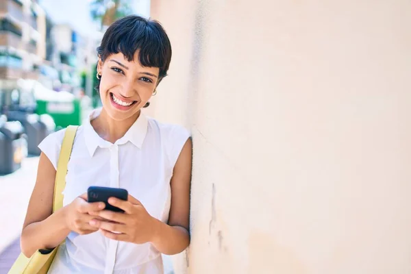 Young woman with short hair smiling happy outdoors using smartphone