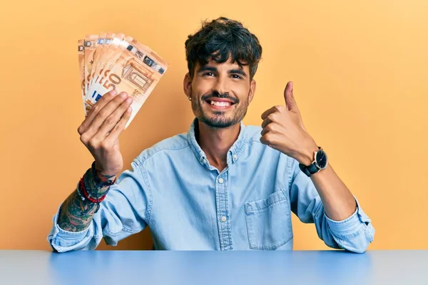 Jovem Hispânico Segurando Notas Euro Sentado Mesa Sorrindo Feliz Positivo — Fotografia de Stock