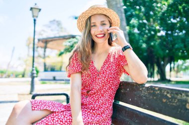 Genç sarışın kadın tatilde. Parktaki bankta oturmuş akıllı telefondan konuşuyor.