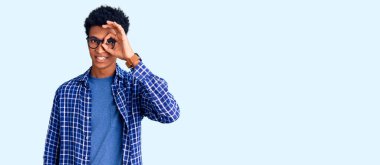 Genç Afro-Amerikan adam günlük kıyafetler ve gözlük takıyor. El hareketleriyle gülümsüyor, gözleriyle mutlu yüzle parmaklarının arasından bakıyor.. 