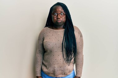 Saçları örgülü, gözlüklü, komik yüzlü, yanakları şişen genç siyahi bir kadın. Havayla şişmiş ağız, çılgın bir ifade.. 