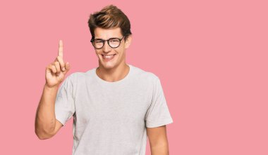 Yakışıklı, beyaz, günlük kıyafetler ve gözlük takan bir numaralı parmağını gösterip onu işaret eden kendine güvenen ve mutlu bir adam.. 