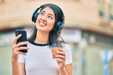 Genç İspanyol kadın kahve içiyor ve şehirde akıllı telefon ve kulaklık kullanıyor..