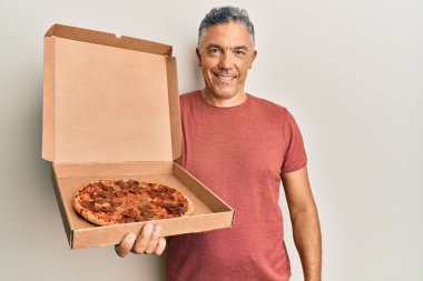 Yakışıklı orta yaşlı olgun bir adam pizza kutusunu tutuyor. Pozitif ve mutlu görünüyor. Kendine güvenen bir gülümsemeyle dişlerini gösteriyor. 