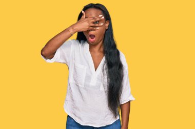 Gündelik kıyafetler giyen genç siyahi kadın şok içinde yüzünü ve gözlerini kapayarak utangaç ifadesiyle parmaklarının arasından bakıyor.. 