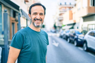 Orta yaşlı, sakallı, açık havada mutlu gülümseyen bir adam.