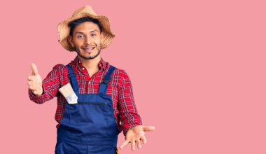 Yakışıklı Latin Amerikalı, tamirci üniforması giyen genç adam kameraya bakıp sarılmak için kollarını açmış gülümsüyor. Mutluluğu kucaklayan neşeli bir ifade.. 