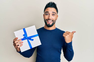 Elinde sakallı genç bir adam baş parmağını yukarı kaldırıyor ve ağzı açık gülümsüyor. 