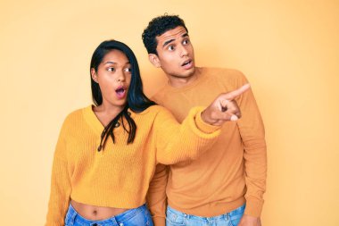 Güzel Latin bir çift, gündelik giysiler giyip parmaklarını gösteriyorlar. İleriyi gösteriyorlar, ağzı açık, şaşkın, ön tarafta bir şey var. 