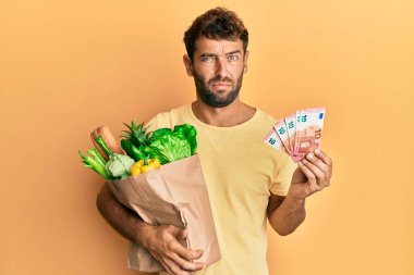 Bakkalda sakalı olan yakışıklı bir adam ve 10 avroluk banknotlar şüpheci ve sinirli, sorun yüzünden somurtuyor. negatif kişi. 